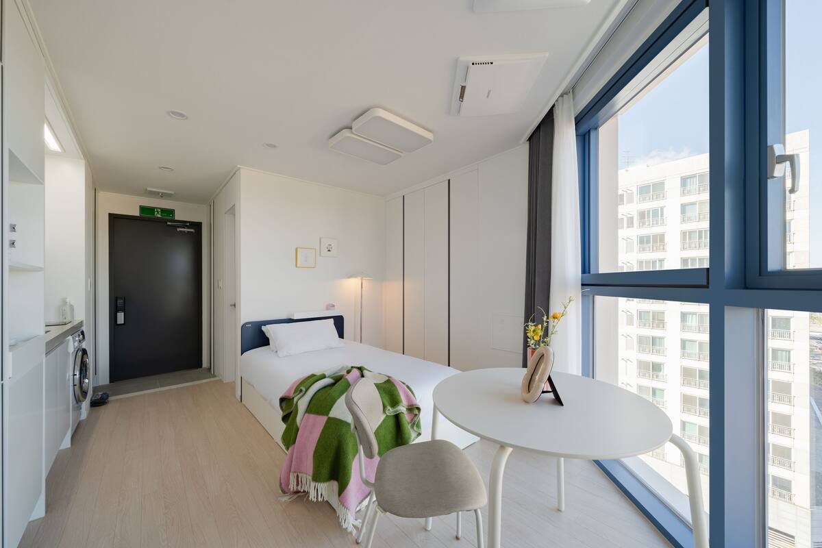 Una habitación de hotel moderna con una cama, una mesa redonda y vistas a la ciudad a través de amplias ventanas.