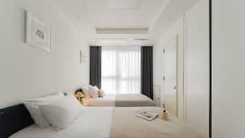 Habitación de hotel con dos camas, un ventanal con cortinas, un cuadro en la pared y una mesita de noche con lámpara y un libro.