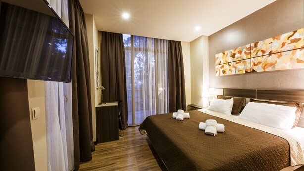 A hotel room with a large bed, a flat-screen TV, a desk, and a window with curtains. - Sani Apart Hotel (Tbilisi)