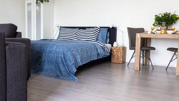 Ein modernes Schlafzimmer mit Bett, einem Holznachttisch, einem Schreibtisch mit zwei Stühlen und einem kleinen Topfpflanzen.