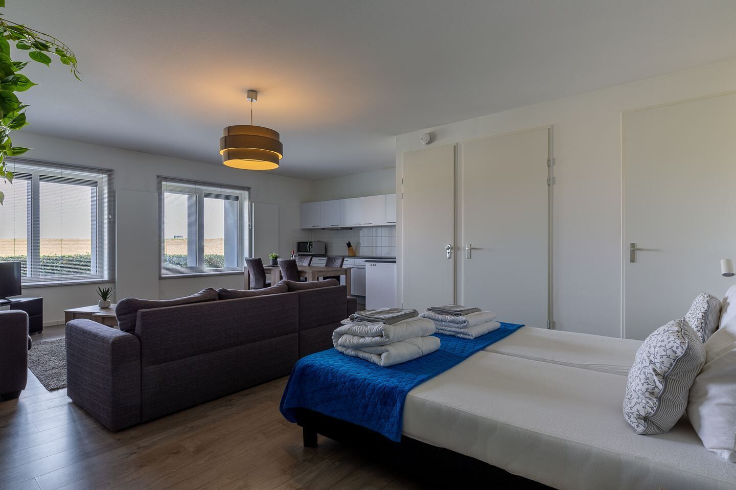 A modern, well-lit room with a bed, a sofa, a dining area, and a kitchen.