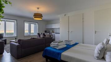 A modern, well-lit room with a bed, a sofa, a dining area, and a kitchen.