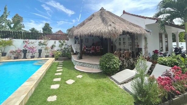 Una casa con techo de paja, piscina y un jardín bien cuidado.