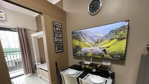 Un coin repas avec une table dressée pour deux personnes, une horloge au mur et un téléviseur diffusant des images panoramiques.