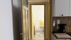 Un pasillo estrecho con baldosas de diseño en el suelo, una puerta de madera y una zona de cocina con cafetera y lavabo.