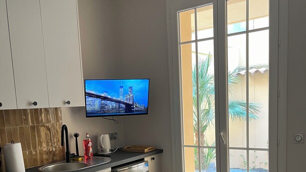 Una cocina equipada con lavavajillas, un televisor de pantalla plana sobre el fregadero y una ventana con vista a palmeras.