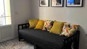 Una habitación con un sofá, baldosas de suelo estampadas, una silla y tres cuadros en la pared.