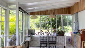 Una cocina con un ventanal grande, un ventilador, dos sillas, una mesa y una lámpara colgante.