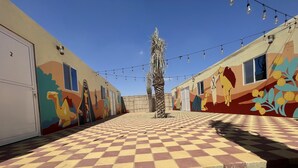 A corridor with a checkered floor leading to a building with colorful murals and string lights. - Easy Trip Desert Camp (Al Awir)