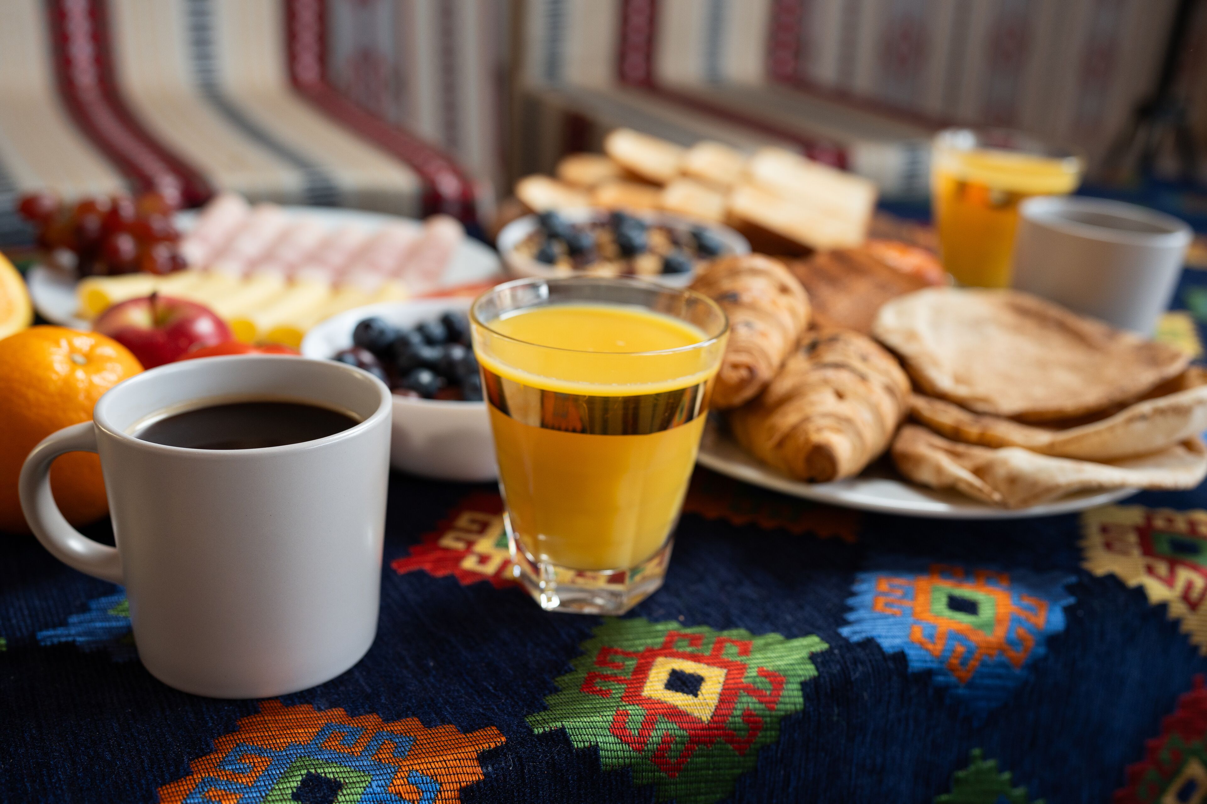Un desayuno con una taza de café, un vaso de jugo de naranja y un plato de pasteles y frutas.