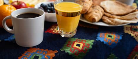 Un desayuno con una taza de café, un vaso de jugo de naranja y un plato de pasteles y frutas.