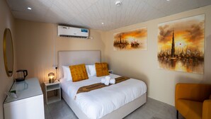 A hotel room with a bed, bedside table, lamp, air conditioning unit, and artwork on the walls. - Easy Trip Desert Camp (Al Awir)
