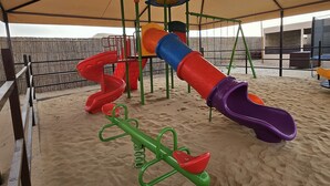 A playground with a sand play area, including a seesaw and slides. - Easy Trip Desert Camp (Al Awir)