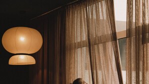 A room with wicker furniture, a large window with sheer curtains, and a hanging light fixture. - 2Places Soul (Loerrach)