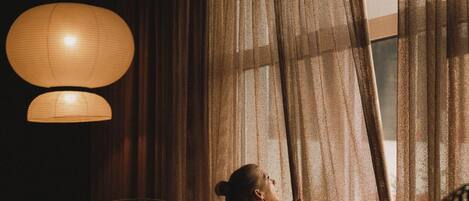 A room with wicker furniture, a large window with sheer curtains, and a hanging light fixture.