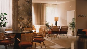 A well-lit, modern living room with a round dining table surrounded by wicker chairs, a sofa, and a large window with sheer curtains. - 2Places Soul (Loerrach)