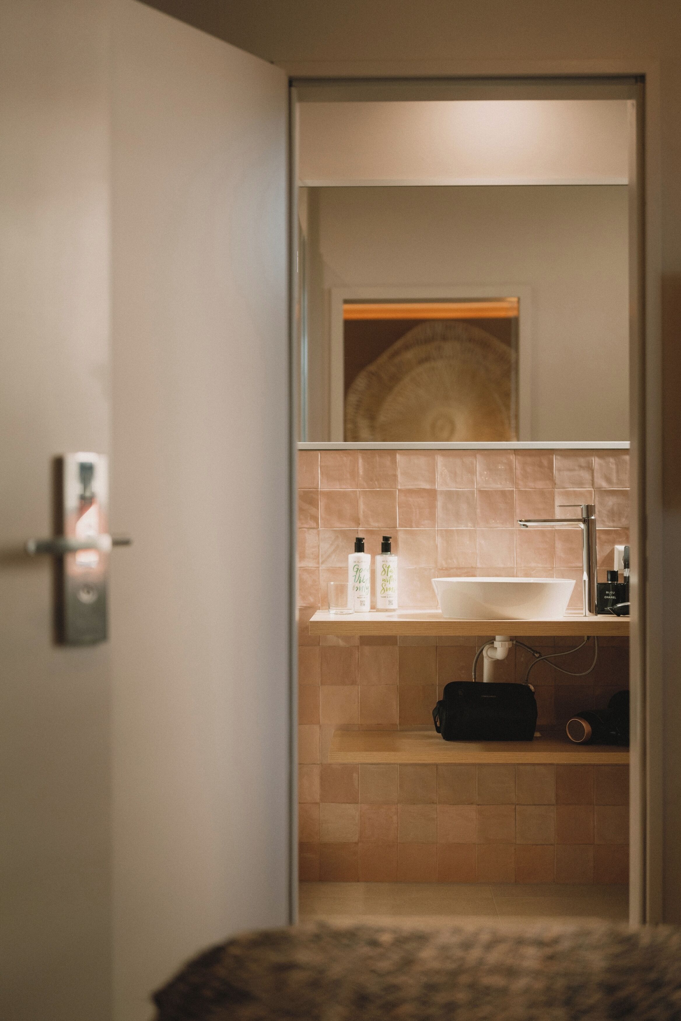 Une salle de bain moderne avec un grand miroir, un lavabo blanc et des carreaux de couleur beige.