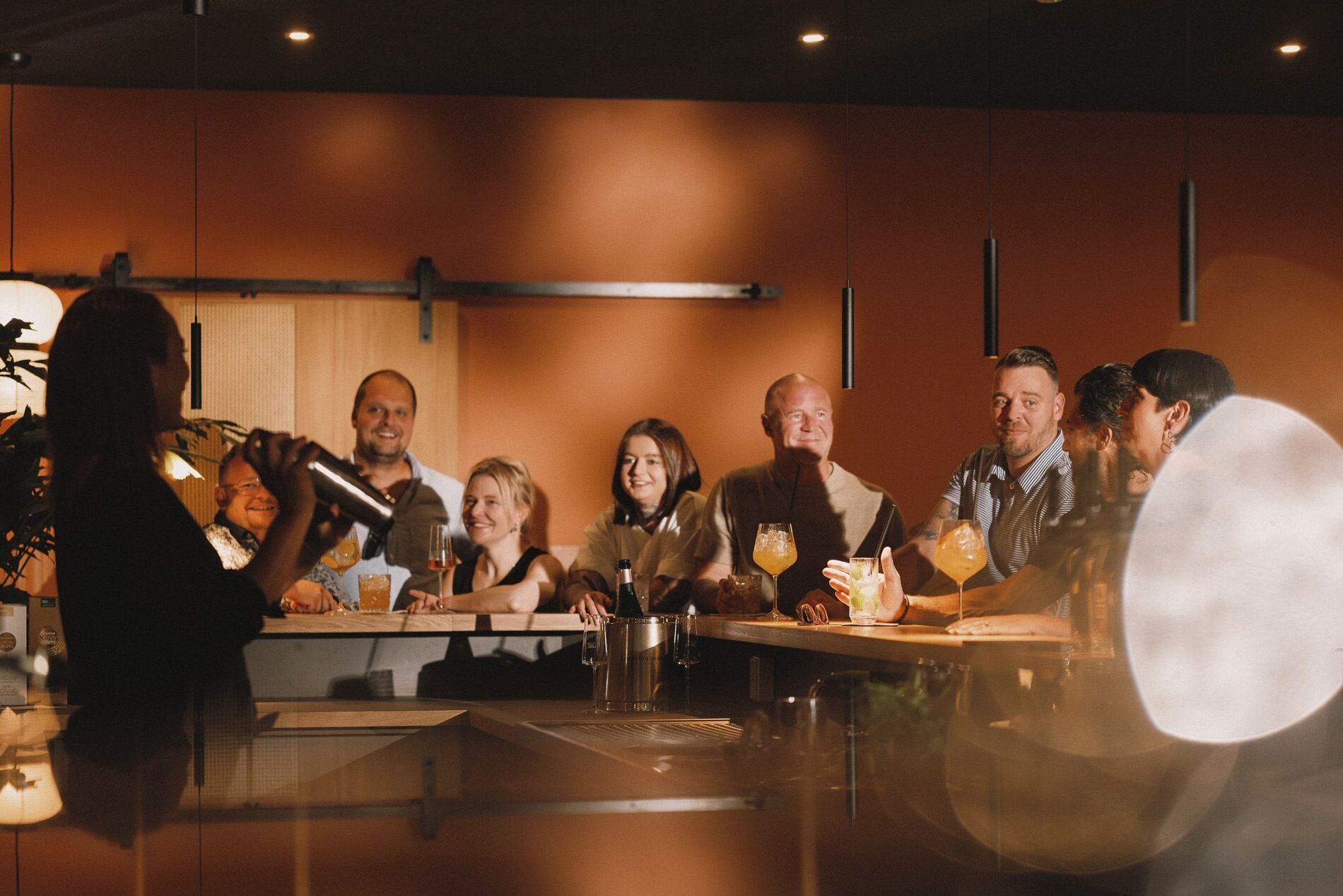 A group of people seated around a bar area with a bartender preparing drinks.