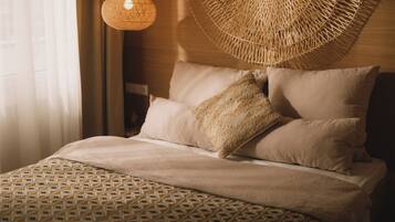 Una cama bien hecha con ropa de cama estampada, un tapiz de pared tejido y una lámpara colgante.