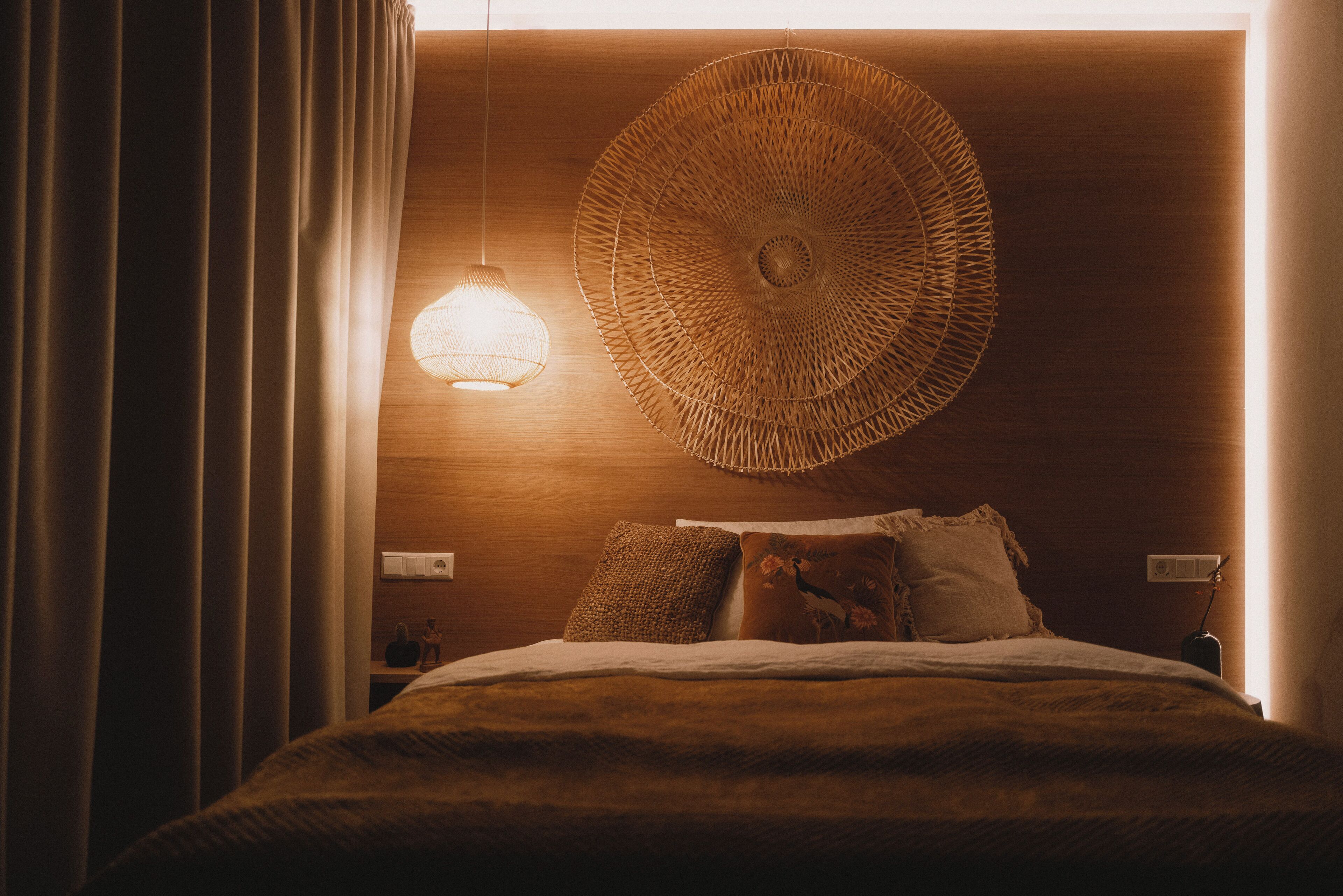 Un lit recouvert d’une couverture à motifs, une tapisserie murale tissée et une suspension lumineuse.