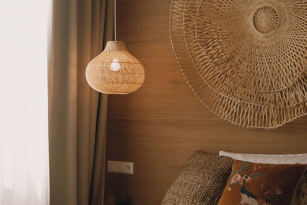 Un dormitorio con una cama, una lámpara colgante tejida, una gran obra de arte tejida en la pared y una almohada texturizada marrón.