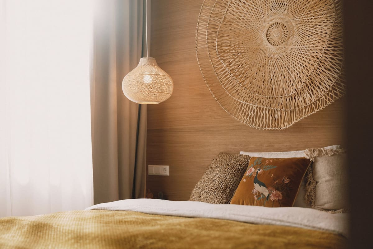 Un dormitorio ordenado con una cama, una lámpara colgante tejida y un adorno de pared tejido.