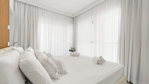 Een moderne hotelkamer met een groot bed, witte lakens en dunne gordijnen.