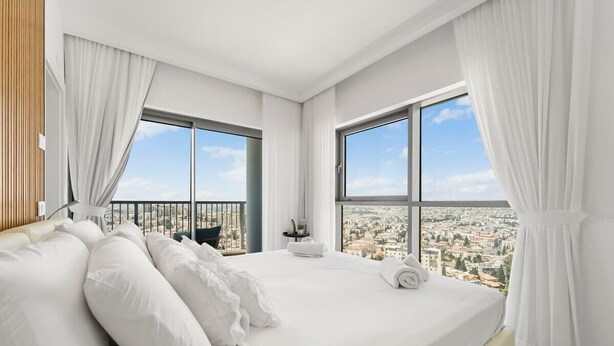 Een moderne hotelkamer met een groot bed, witte linnens en uitzicht op de stad door ramen van de vloer tot aan het plafond.