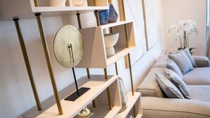 Een moderne woonkamer met een beige bank, een wit wandrek met decoratieve objecten, en een ronde wandklok.