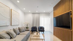 Een moderne woonkamer met een bank, twee fauteuils, een salontafel en een televisie.
