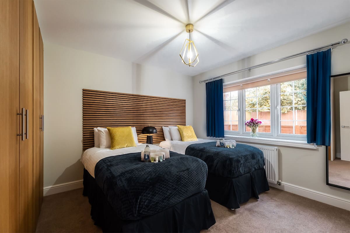 A hotel room with two beds, a wooden headboard, a large window with curtains, and a ceiling fan.