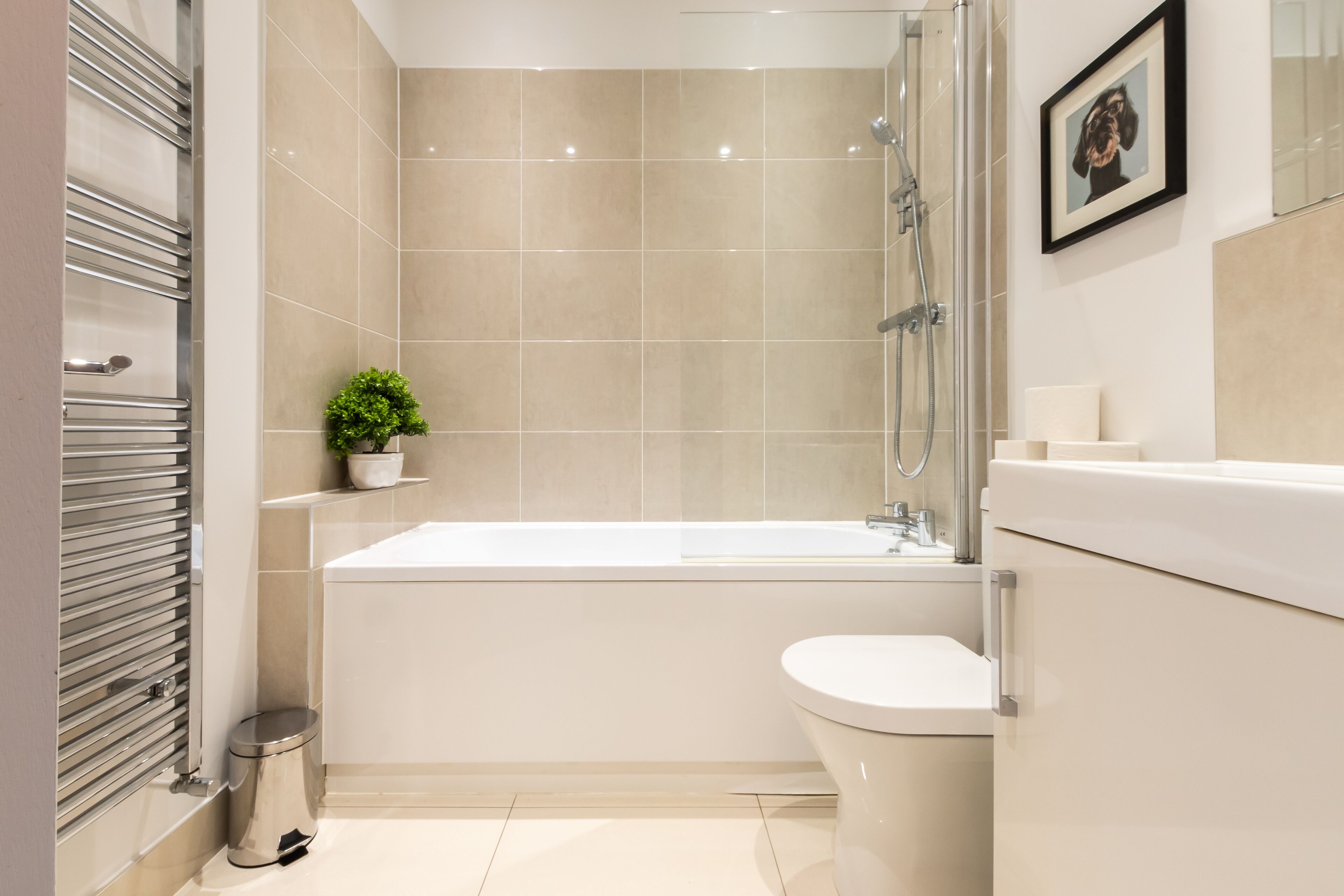A modern bathroom with a bathtub, toilet, and a small potted plant.
