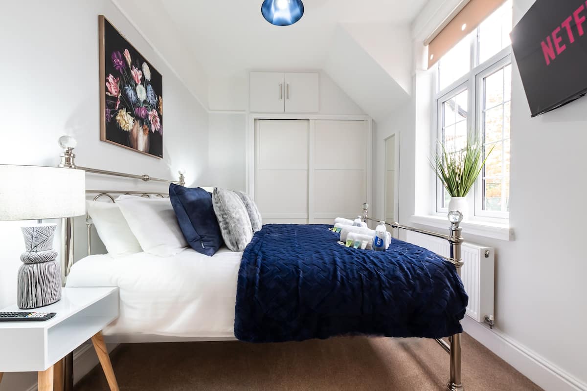 A neatly arranged bedroom with a bed, bedside table, lamp, and a window with a view.