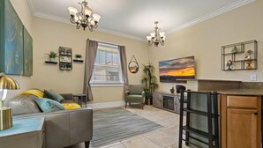 Ein Wohnzimmer mit einer Couch, einem Couchtisch und einem Fernseher. Es gibt eine Küchenzeile mit Schränken und einer Arbeitsplatte.