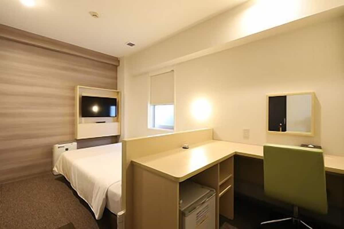 Une chambre d’hôtel équipée d’un lit, d’un bureau, d’une chaise, d’une télévision et d’un miroir.