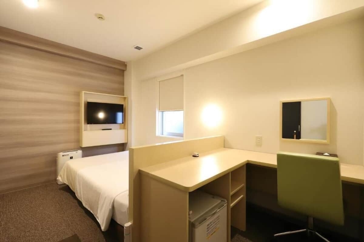 Une chambre d’hôtel avec un lit, un bureau, une chaise, une télévision et une fenêtre.