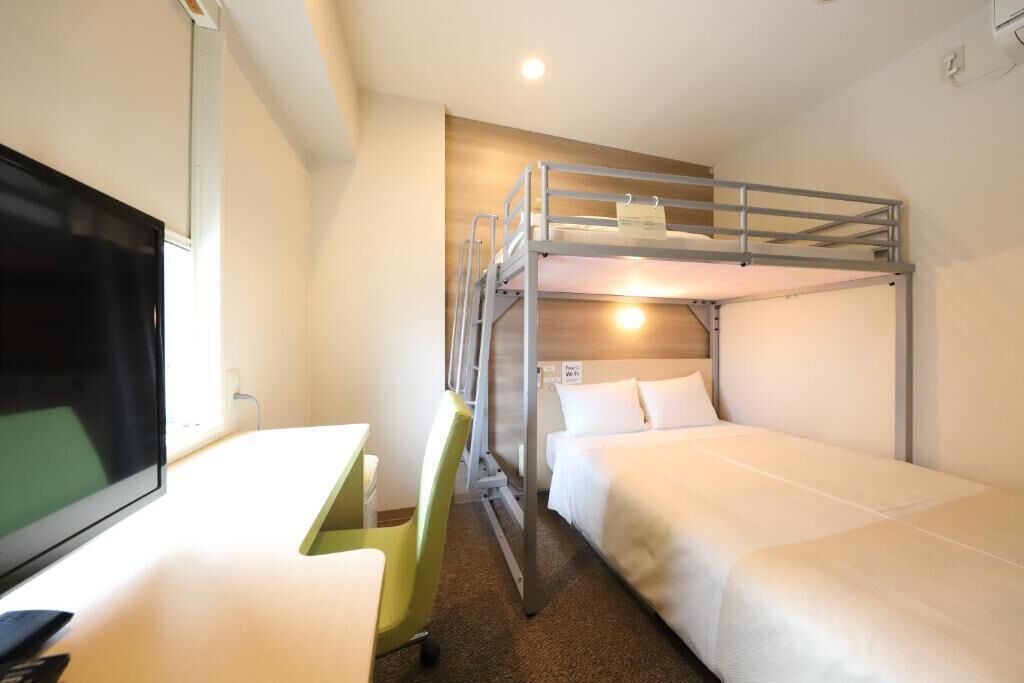A hotel room with bunk beds, a desk, and a television.