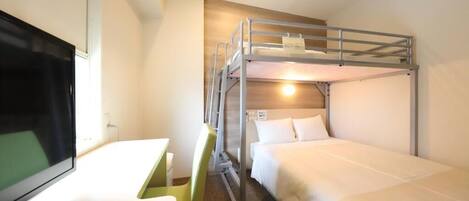 A hotel room with bunk beds, a desk, and a television.