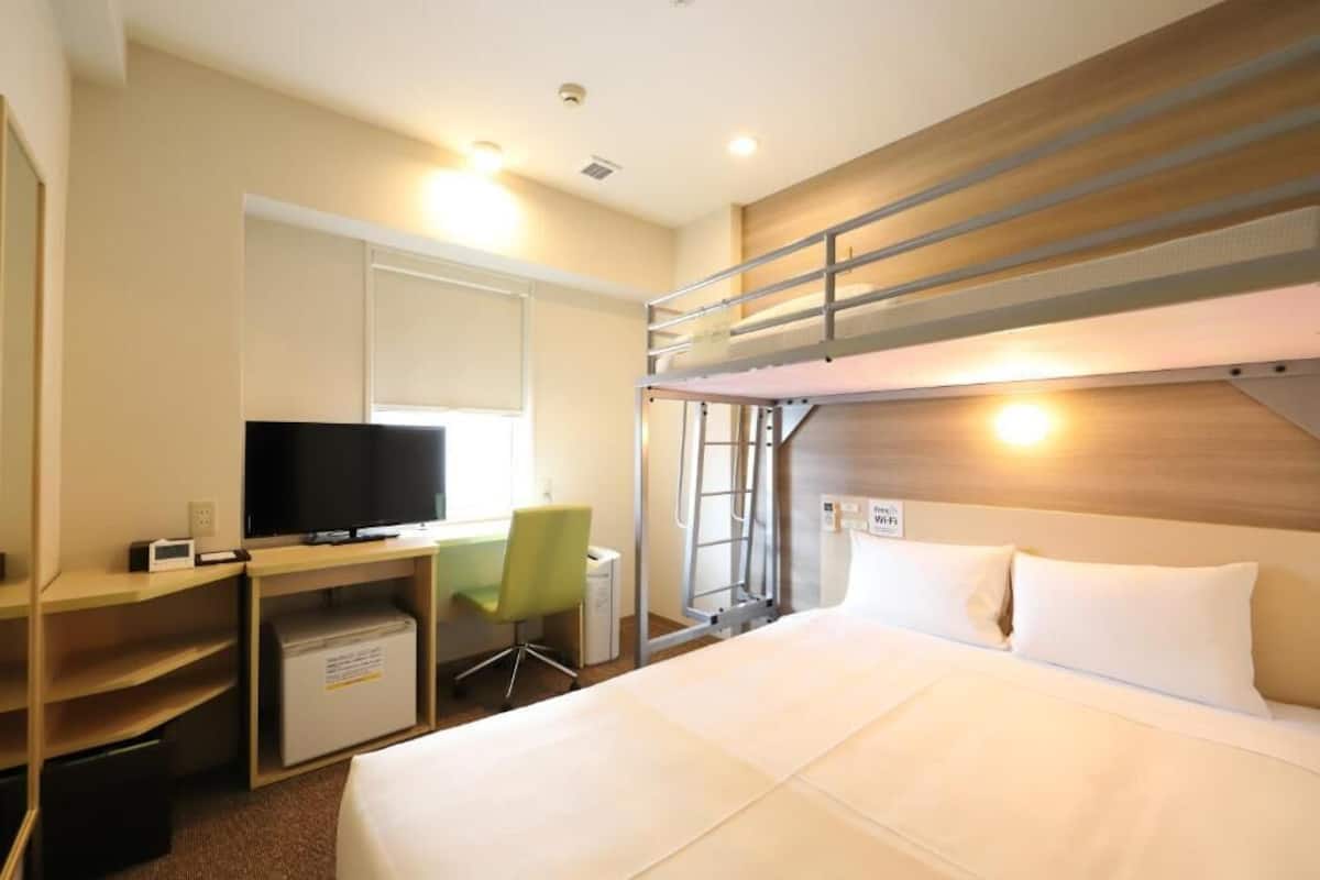 Une chambre d’hôtel avec un lit superposé, un bureau avec une télévision et une chaise.