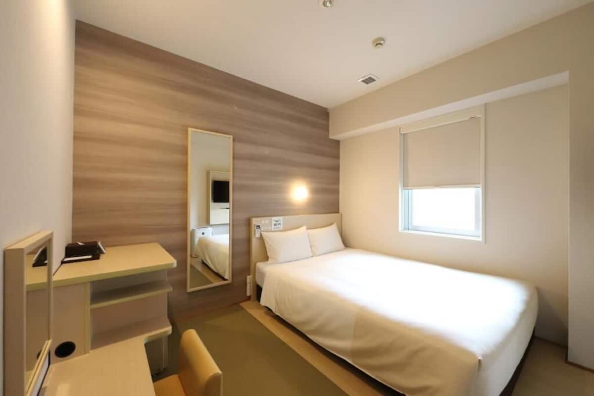 Une chambre d’hôtel moderne équipée d’un lit simple, d’un bureau, d’une chaise et d’un grand miroir.