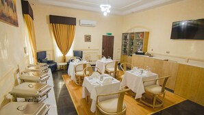 Comedor de hotel con varias mesas dispuestas para el servicio, una barra de buffet y una zona de bar con televisor.