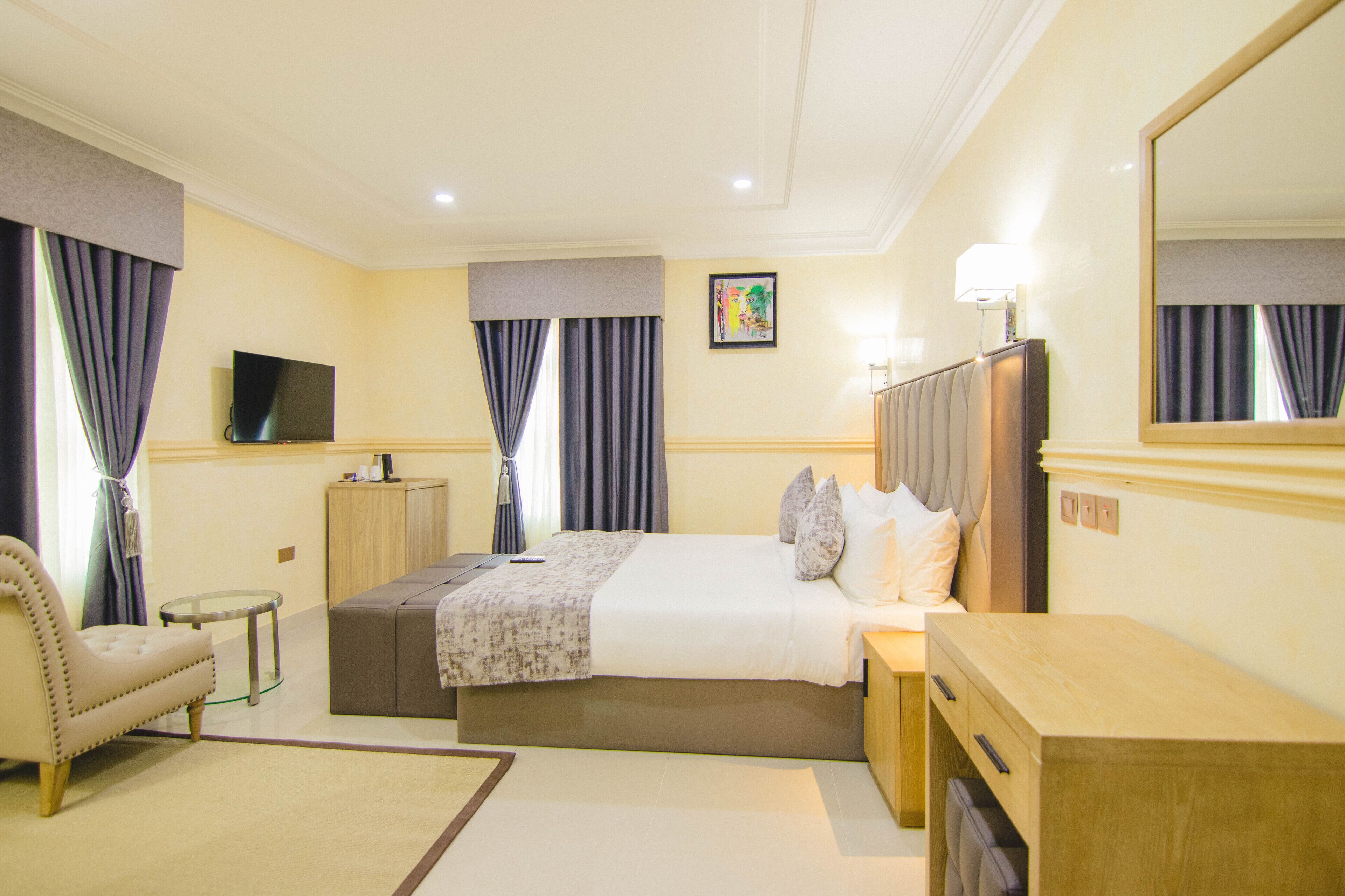 A hotel room with a large bed, a bedside table, a chair, a TV, and a mirror.