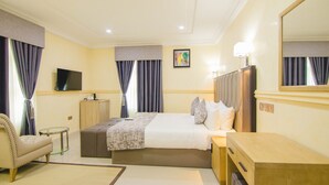 Habitación de hotel con una cama grande, una mesita de noche, una silla, un televisor y un espejo.