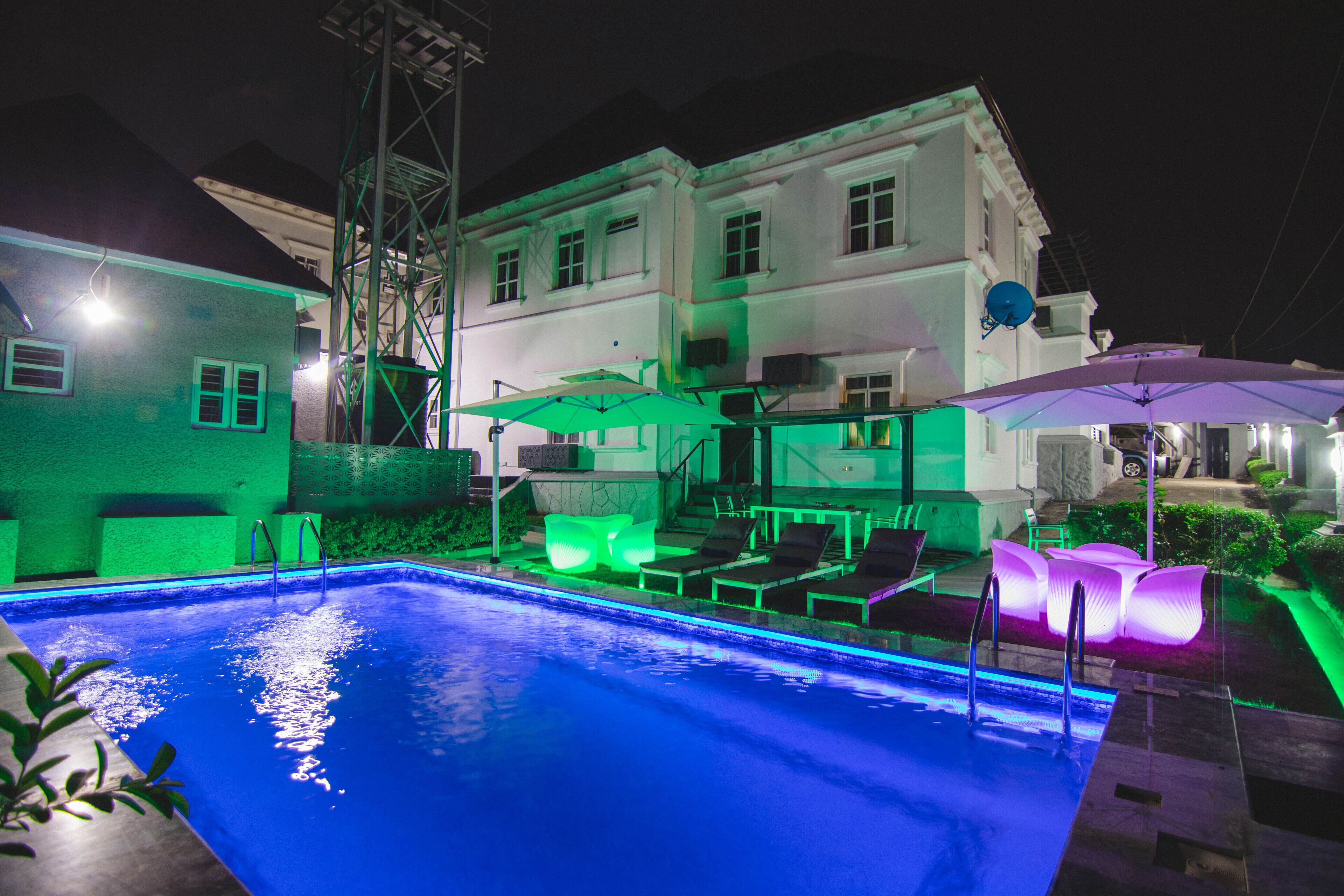 A swimming pool with lounge chairs and umbrellas, surrounded by a building with multiple windows and a satellite dish.