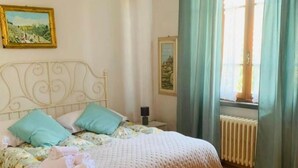 A bedroom with a bed, a nightstand, a lamp, and a window with curtains. - Eno 's house (Lucca)