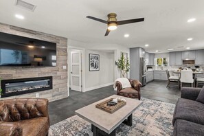 A modern living room with a fireplace, leather armchairs, a coffee table, and a ceiling fan.