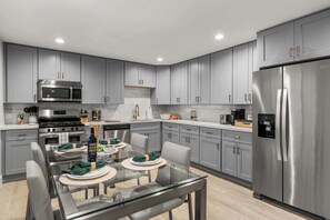 A modern kitchen with grey cabinets, stainless steel appliances, and a glass dining table set for four.