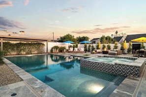 A swimming pool with a geometric tile border, surrounded by outdoor seating and umbrellas.