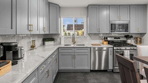A modern kitchen with grey cabinets, stainless steel appliances, and a window with a view of the outside. - Montecito Luxe: 3-Villa Retreat w/ Pool Courtyard (Phoenix)