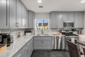 A modern kitchen with grey cabinets, stainless steel appliances, and a window with a view of the outside. - Montecito Luxe: 3-Villa Retreat w/ Pool Courtyard (Phoenix)